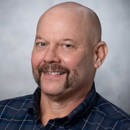 Middle aged white male with shaved head and handlebar moustache.